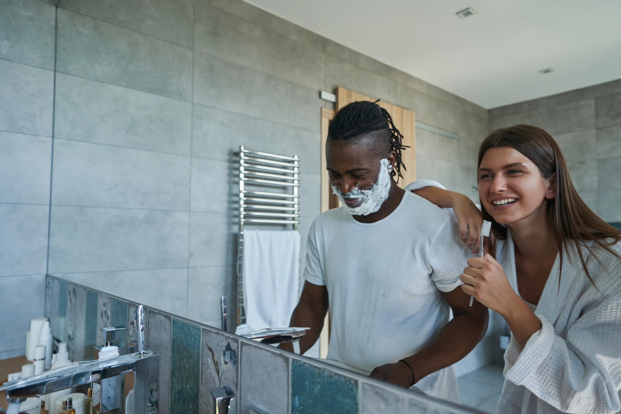 Smiling lady examining foam on male face standing before mirror